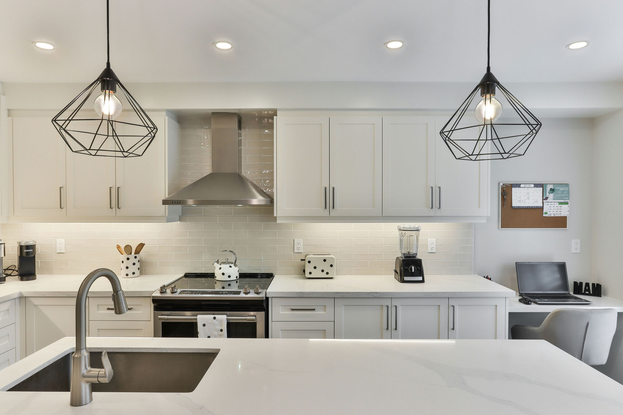 White shaker kitchen with a marble-look island, a stainless hood and black wire pendants