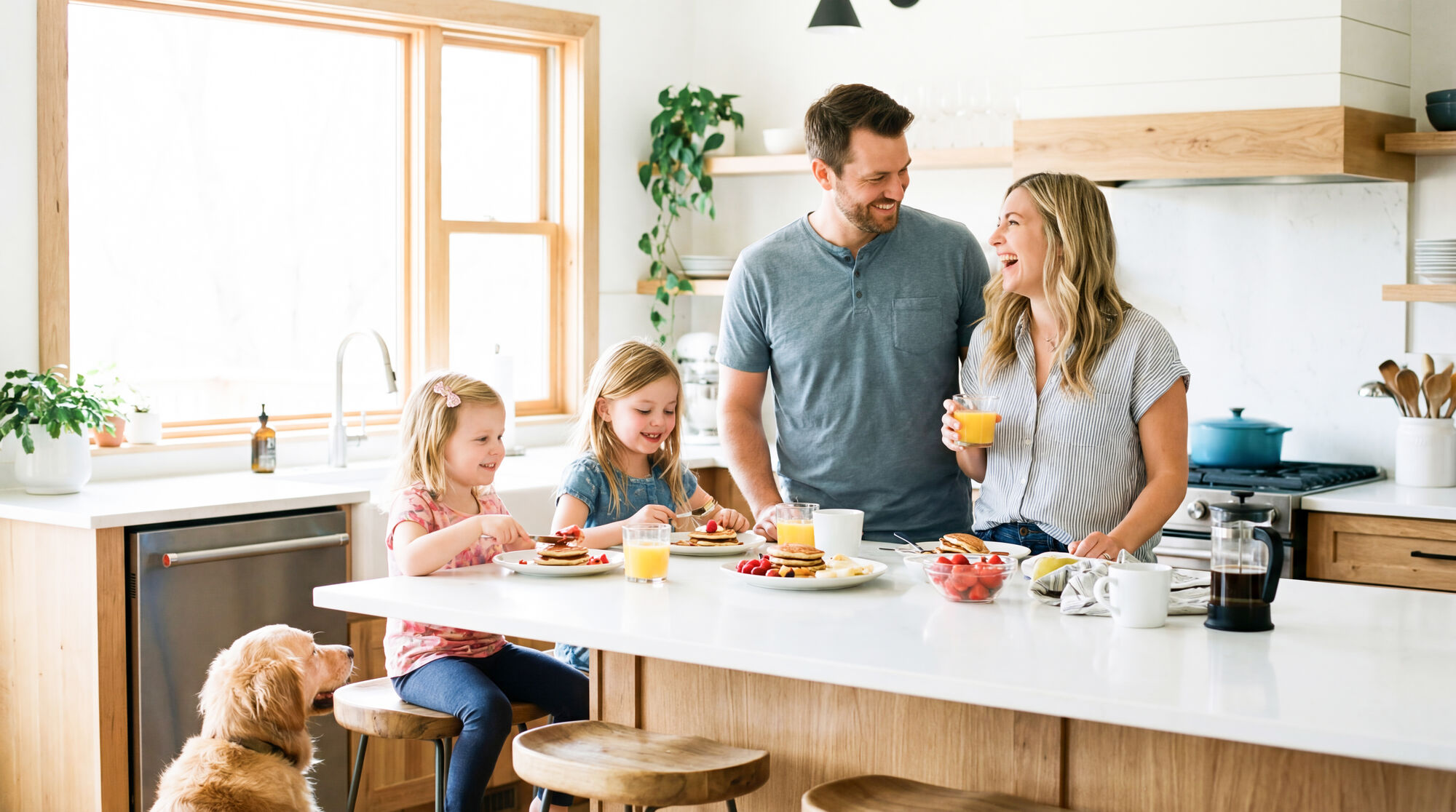 Family having breakfast at a white kitchen island while the dog waits for crumbs