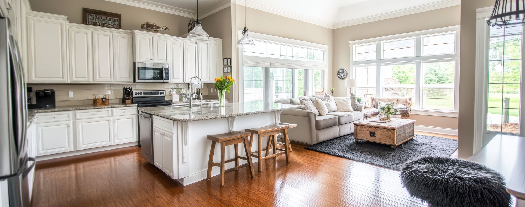 Open living room and kitchen with a white island, wood floors and big windows